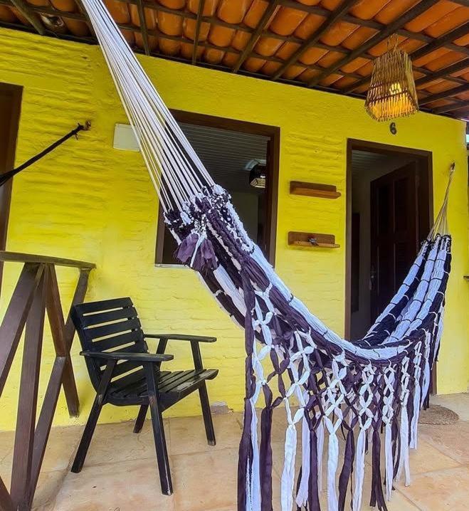 a hammock and a chair in front of a yellow house at Eco Hostal Yuaiurú in Trairi
