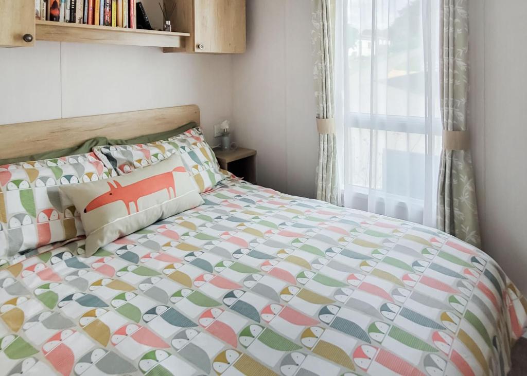 a bedroom with a bed with a comforter and a window at Gorselands Caravan Park in Dorchester