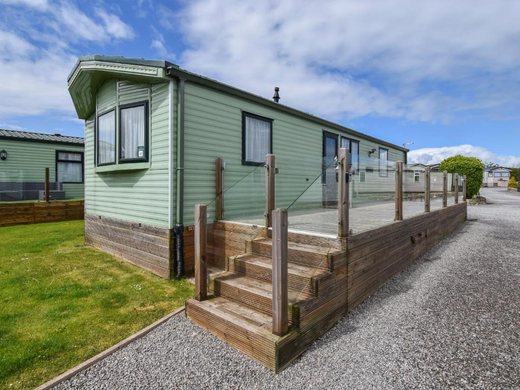 a green house with a wooden porch and stairs at Fellside Lodge in Cockermouth