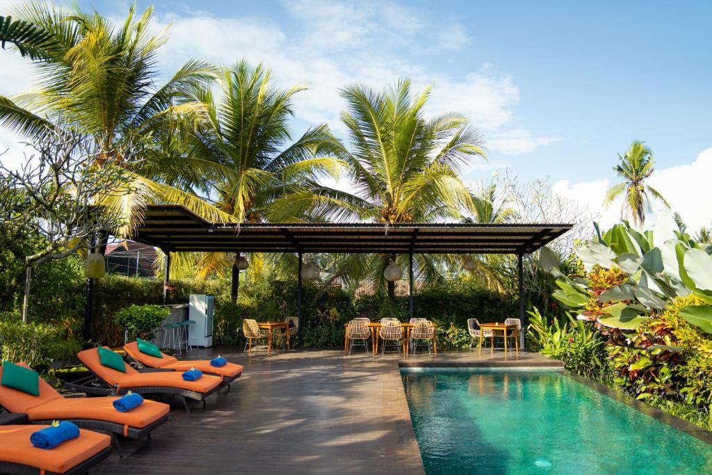 a resort with a pool and chairs and palm trees at Villa Tegal Tis Ubud in Payangan