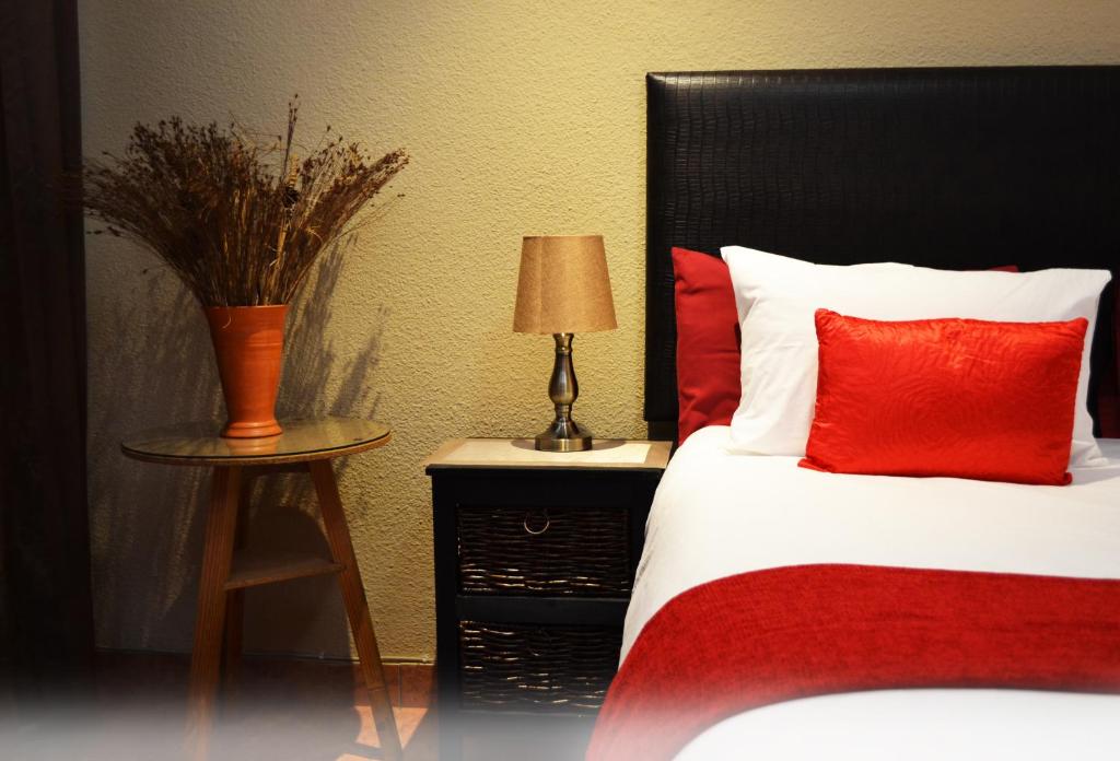 a bed with red and white pillows and a table with a lamp at Kayalako on 4th Avenue in Benoni