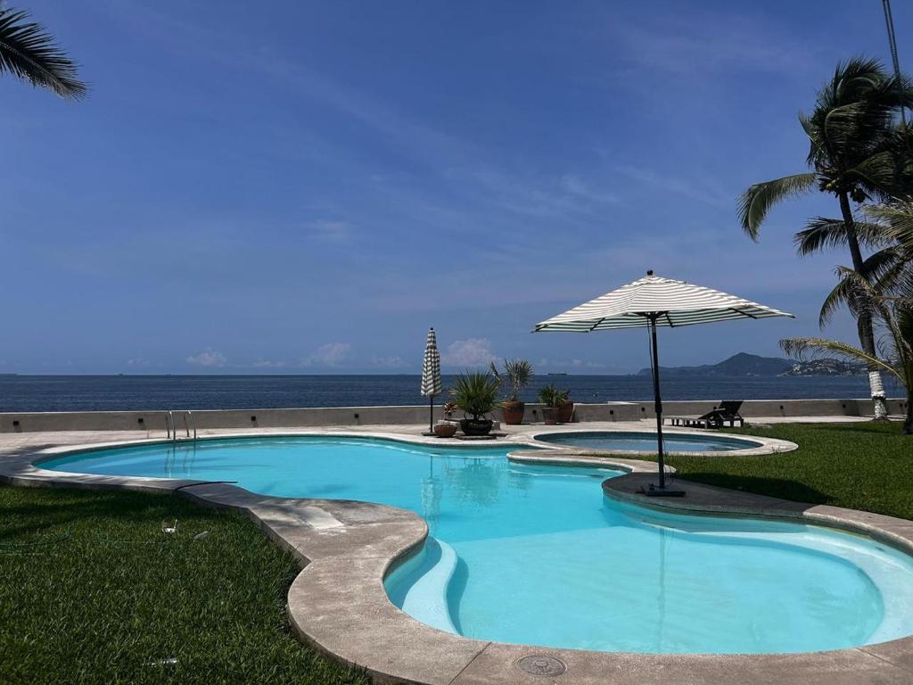 a swimming pool with an umbrella next to the ocean at Condominio Los Corales in Manzanillo