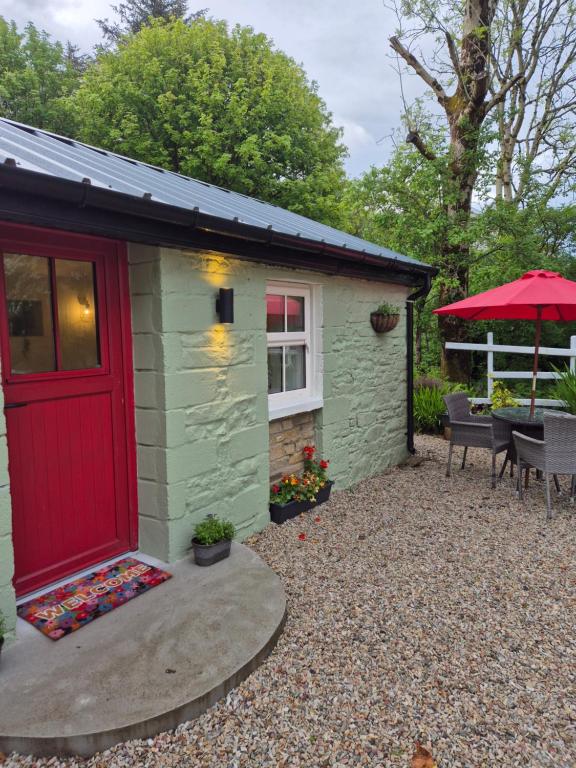 a small green building with a red door and a patio at Waterfall Cottage in Killybegs