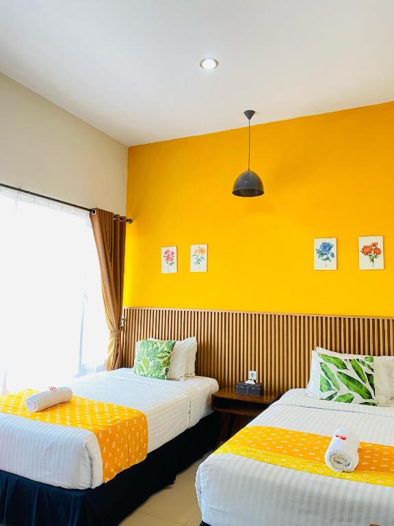 two beds in a room with yellow walls at Omah Manis in Yogyakarta