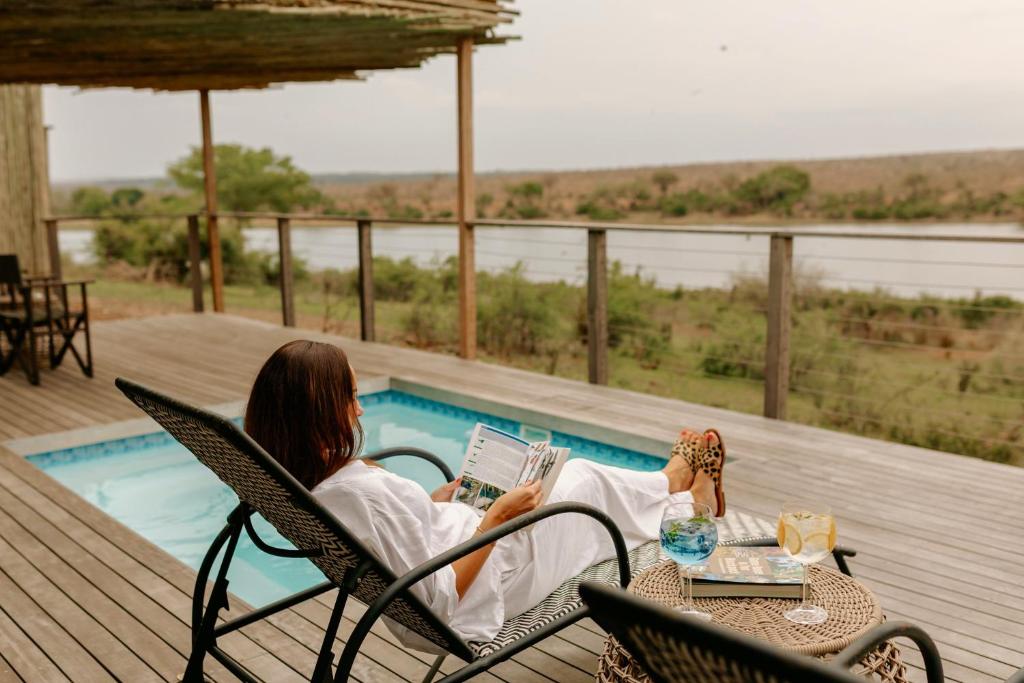 a woman sitting in a chair reading a book by a pool at Buhala Lodge in Malelane