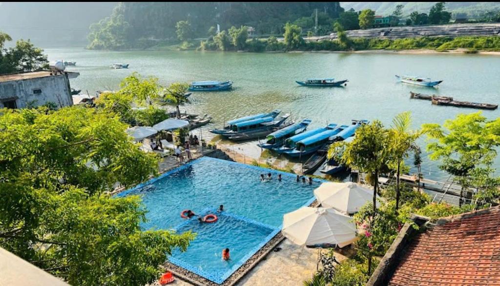 a large swimming pool next to a river with boats at Jade River Phong Nha in Phong Nha
