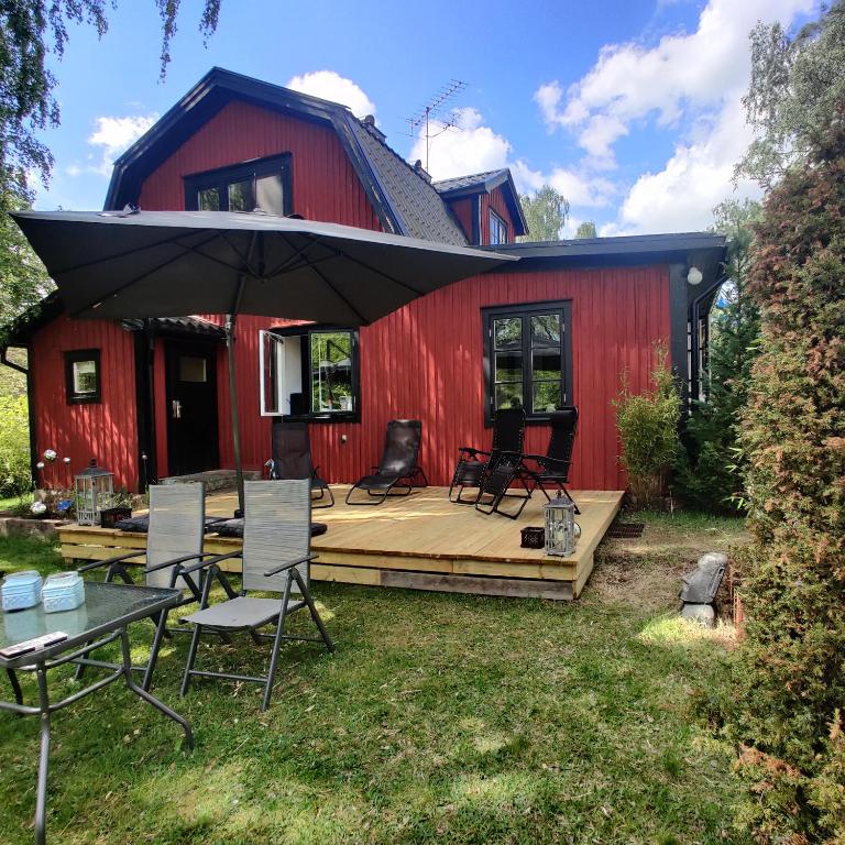 a deck with chairs and an umbrella in front of a red barn at Villa Björkbacka in Vena