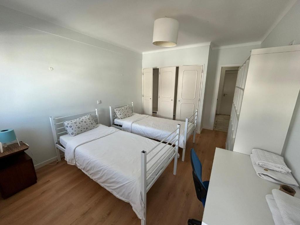 a white bedroom with two beds and a desk at Sal Guest House in Costa da Caparica