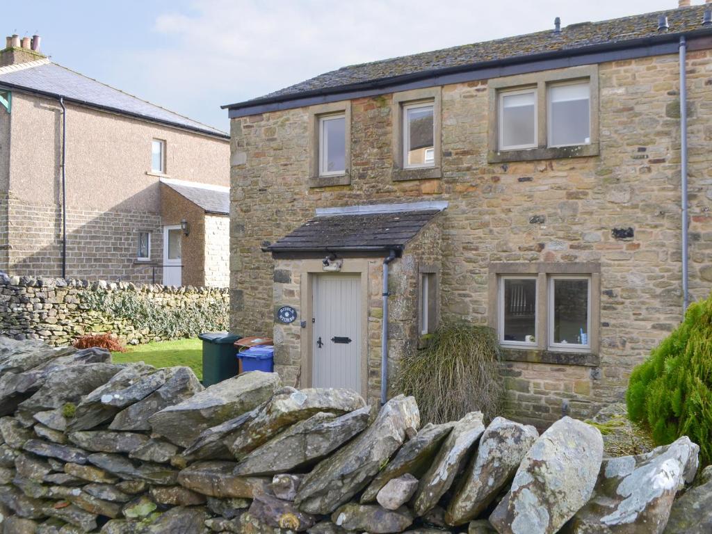 a stone house with a white door and a stone wall at Ribblestones in Austwick