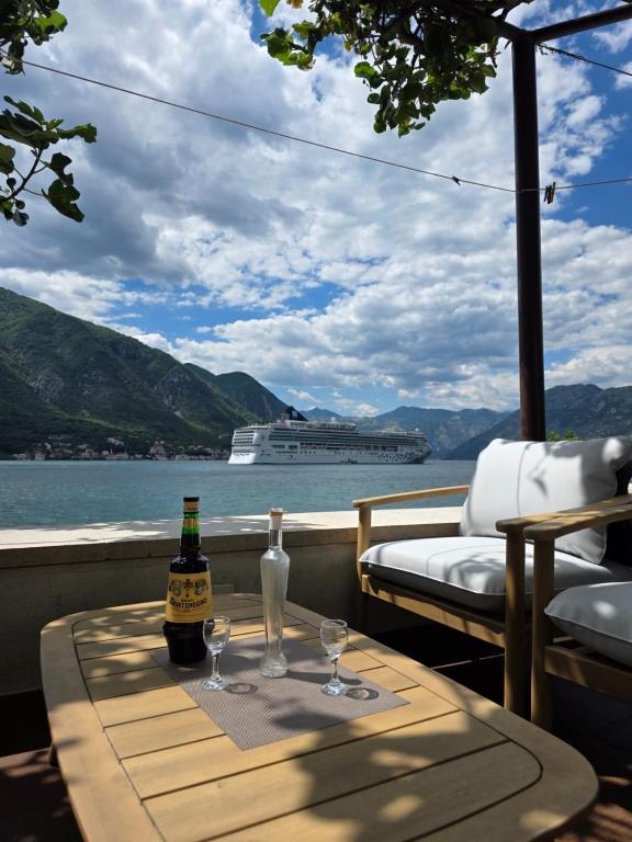 a table with two bottles and glasses on a balcony with a cruise ship at Studio Scala in a seaside house in Dobrota