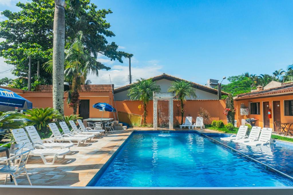 a swimming pool with white chairs and a house at Pousada Acqua Bella PISCINA CLIMATIZADA in Bertioga