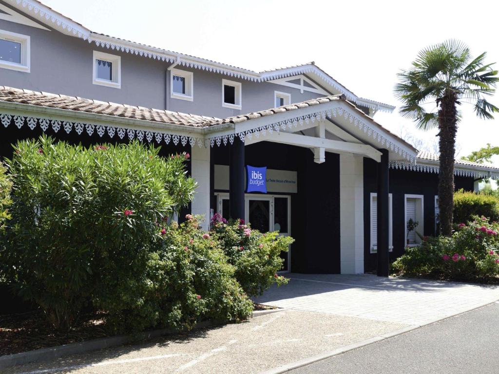 a building with a palm tree and bushes at ibis Budget La Teste Bassin d'Arcachon in La Teste-de-Buch