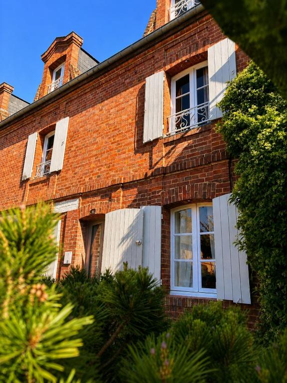 a red brick building with white shuttered windows at La Maison Harmony in Beuvron-en-Auge