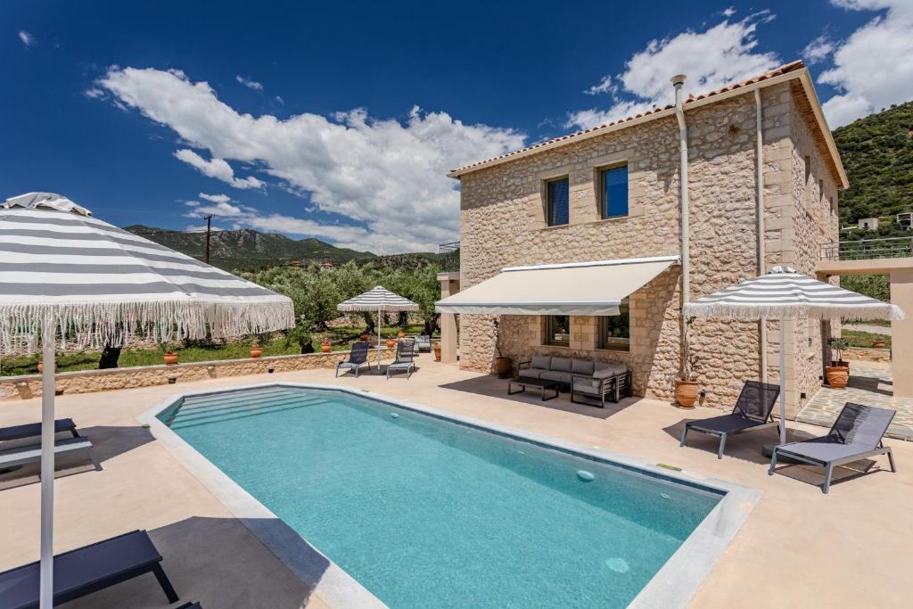 a pool in front of a house with umbrellas at The Olive Grove Kardamyli in Kardamyli
