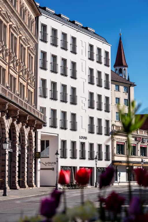 ein großes weißes Gebäude mit einem Uhrturm an einer Straße in der Unterkunft Louis Hotel in München