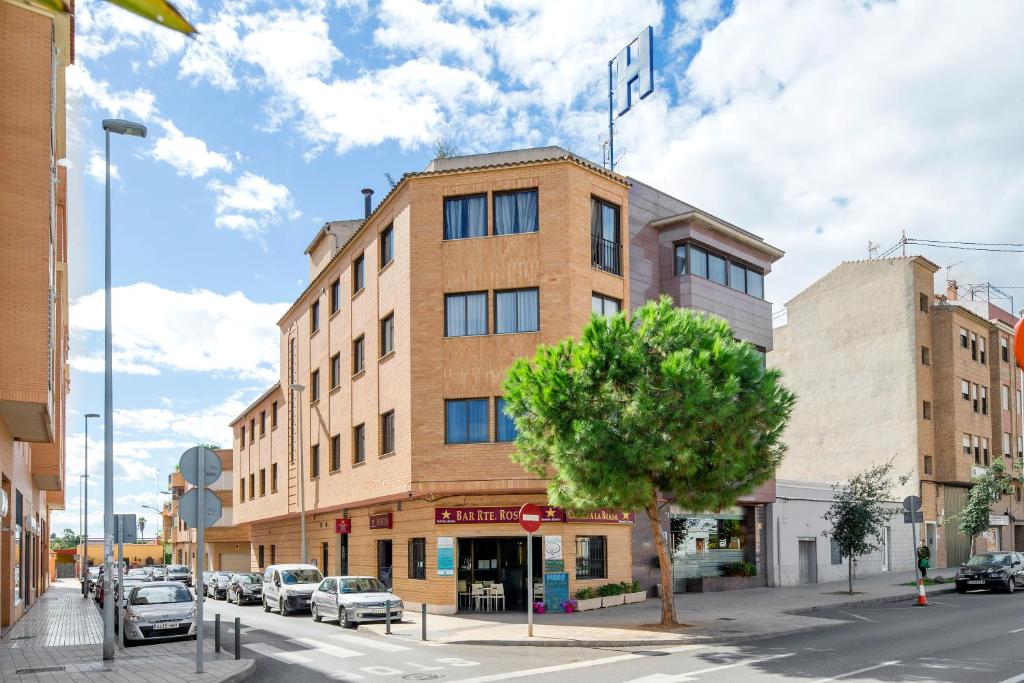 un grand bâtiment en briques sur une rue de la ville avec un arbre dans l'établissement Hotel Rostits, Castellón de la Plana