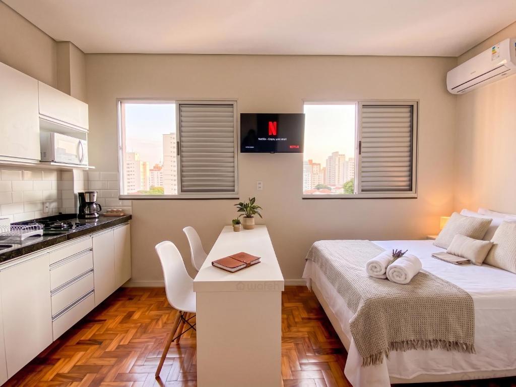 a bedroom with a bed and a kitchen with windows at Prado Premium Lofts e Kitnets com Ar-Condicionado e TV Smart in Belo Horizonte