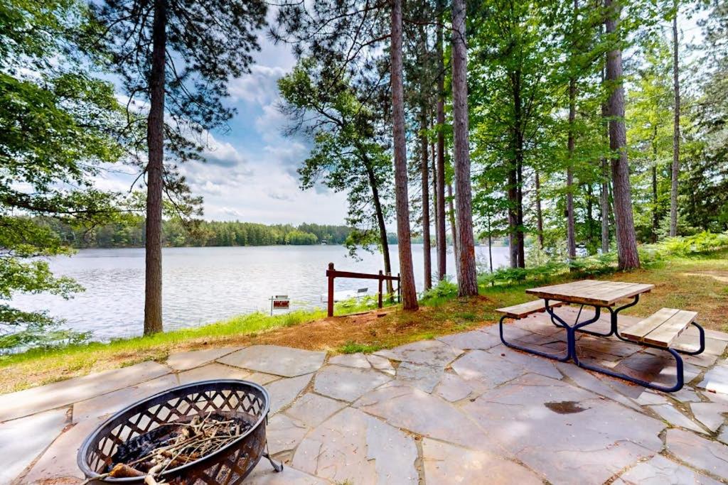 a picnic table and bench next to a lake at Pickerel Point Home in Saint Germain