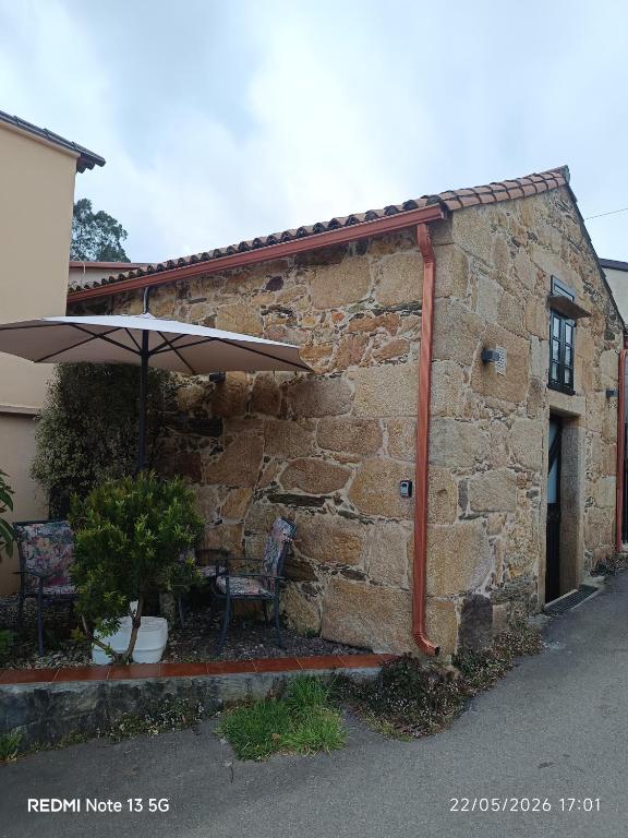a stone building with an umbrella and two chairs at "la Casita" in Boiro