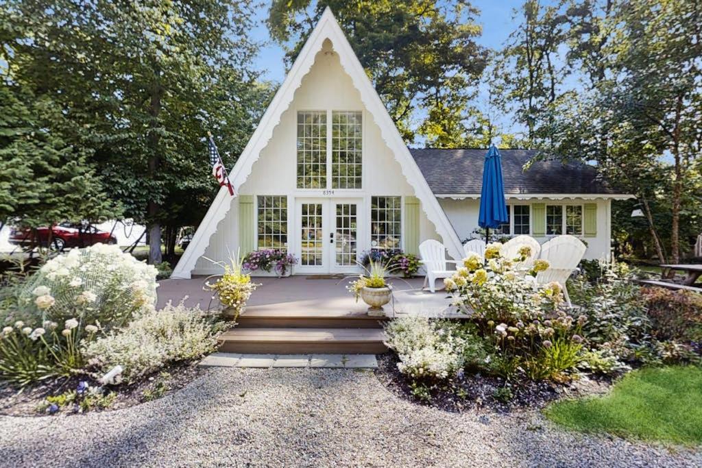 a white house with a porch and chairs and flowers at Mt McSauba A Frame Cottage in Charlevoix