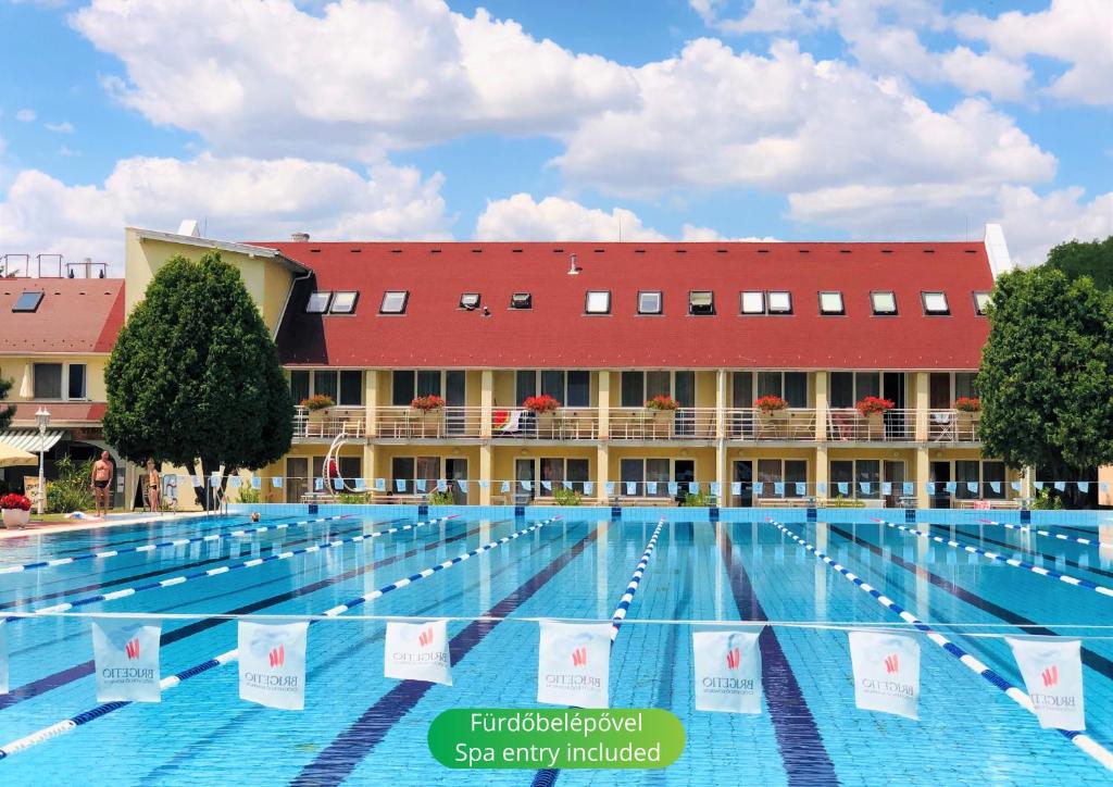 a large swimming pool with a red building in the background at Hét Vezér Apartmanhotel in Komárom