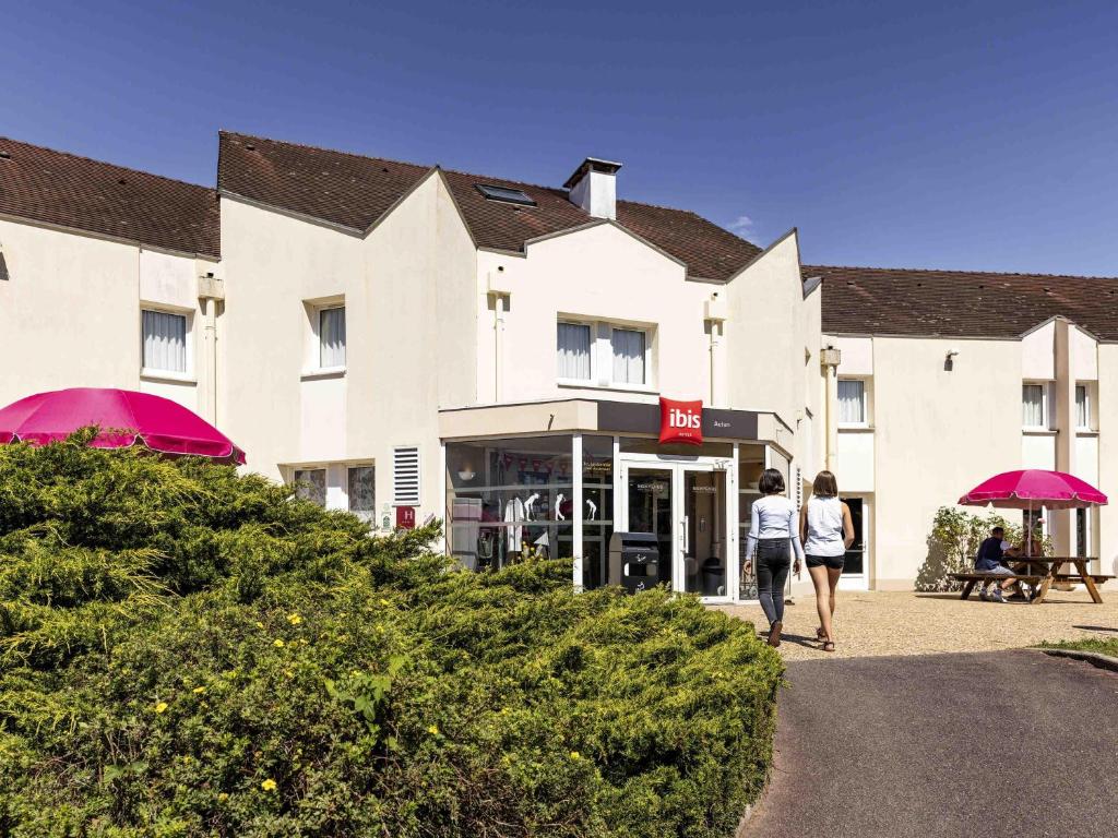 two people walking in front of a hotel with purple umbrellas at Hotel ibis Autun in Autun