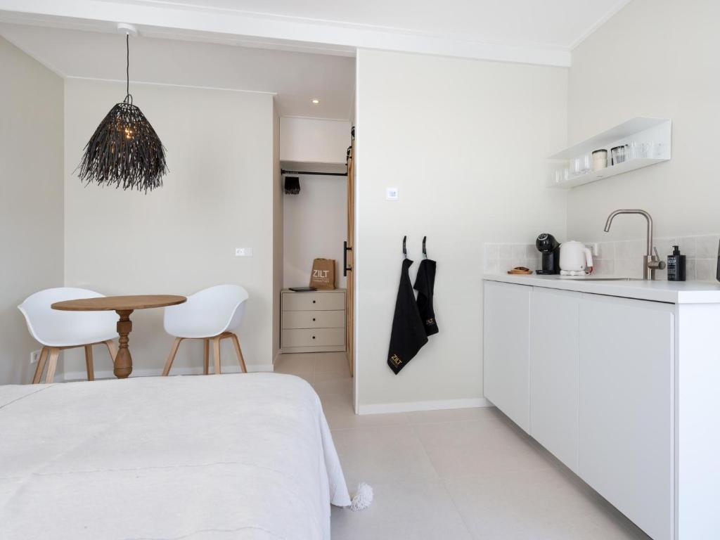 a white kitchen with a bed and a table at Duinsuite in Oostkapelle