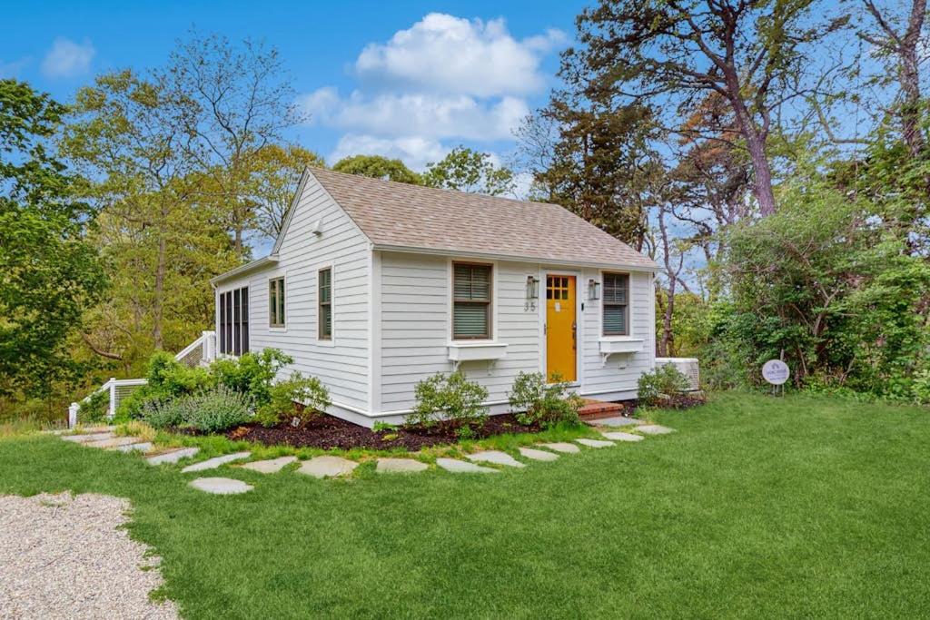 a small white house with a yellow door in a yard at The Saffron Cottage in Wellfleet