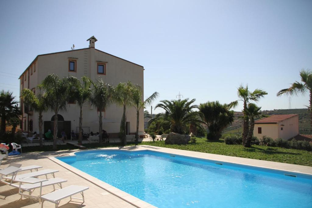 a swimming pool in front of a building with palm trees at Tenute Piazza Countryhouse in Ribera