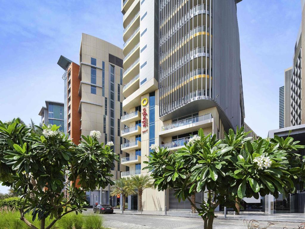 a tall building with trees in front of it at Adagio Abu Dhabi Al Bustan in Abu Dhabi