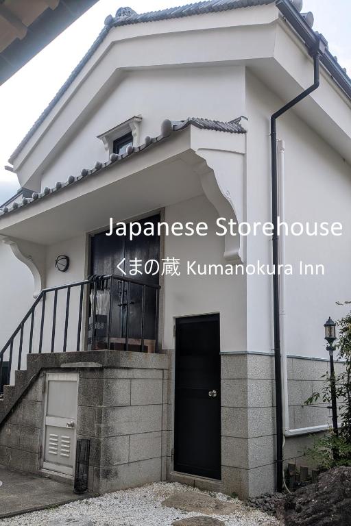 a white house with a black door and stairs at くまの蔵 Kumanokura inn Storehouse in Shingū