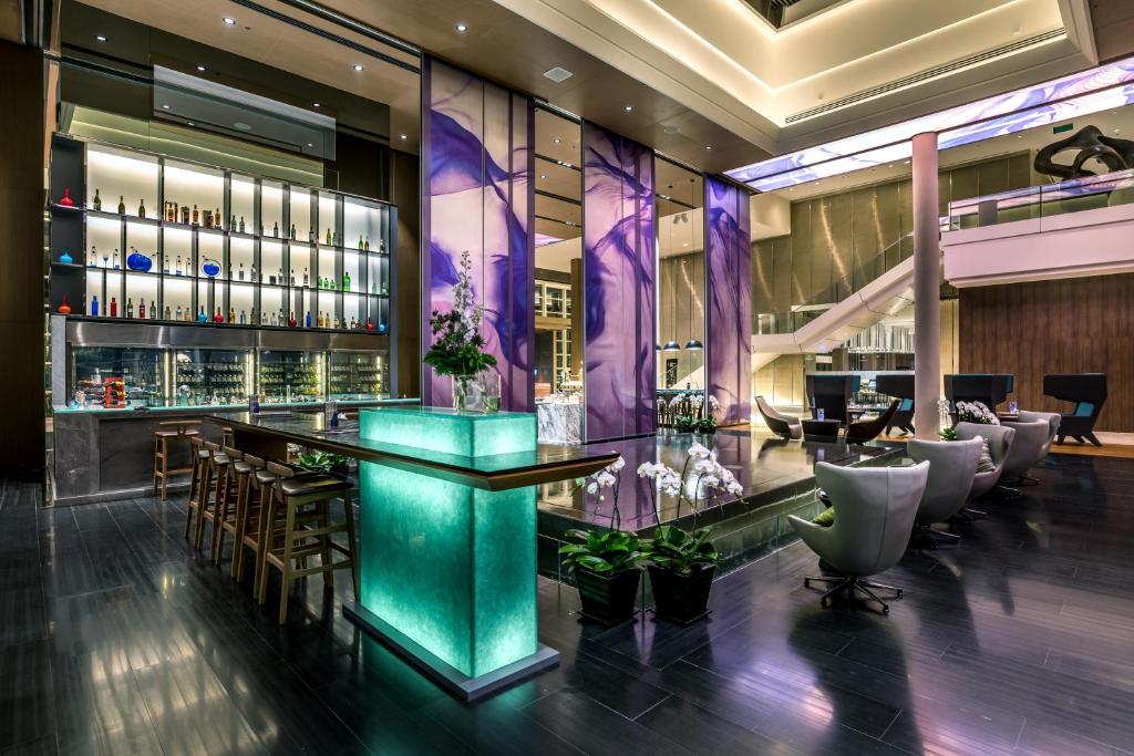 A lobby bar with stools sits beside a glowing central counter and lounge seating.