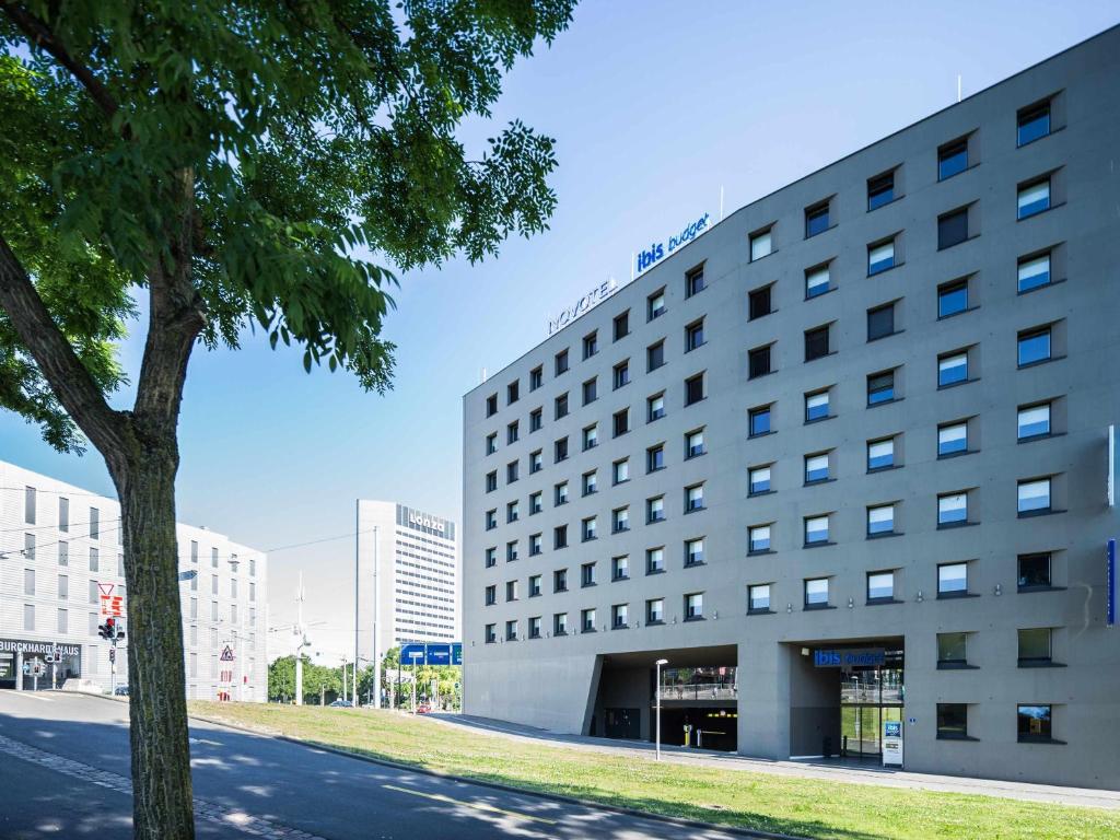 a building with a tree next to a street at ibis budget Basel City in Basel