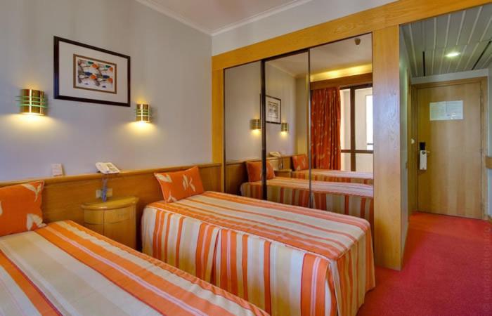 A traditional twin room with striped bedding, mirrored wardrobes and a compact bedside table.