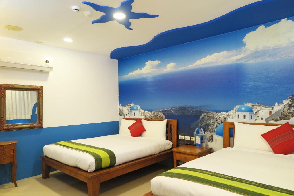 two beds in a room with a mural of santorini at Kenting Sin Sin Hotel in Kenting