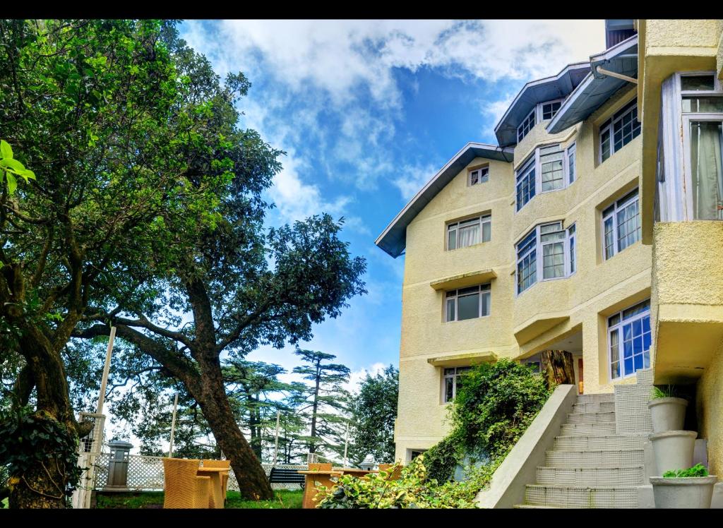 a yellow building with stairs next to a tree at Summit Le Royale Hotel, Shimla in Shimla