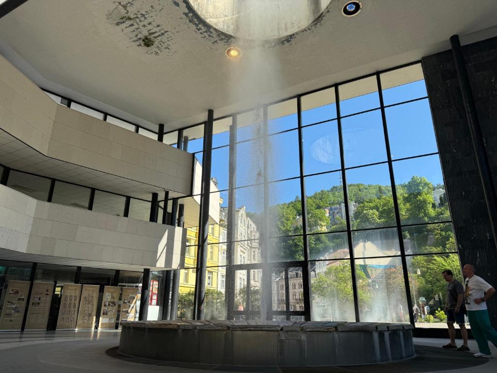 a building with a fountain in front of a large window at Oasis Valley Karlovy Vary Center in Karlovy Vary