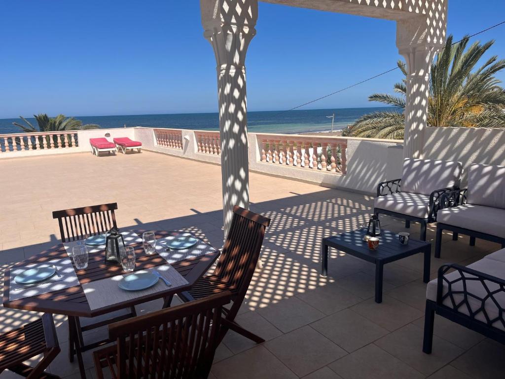 a patio with a table and chairs and the beach at Villa pieds dans l'eau, magnifique terrasse face à la mer in Zarzis