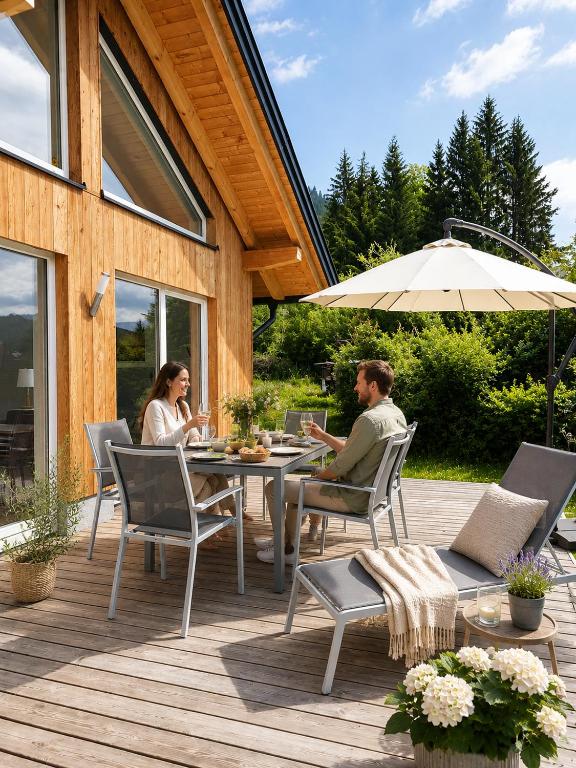 a man and woman sitting at a table on a deck at Ferienhäuser Seetraum - Premium Card inklusive in Weissensee