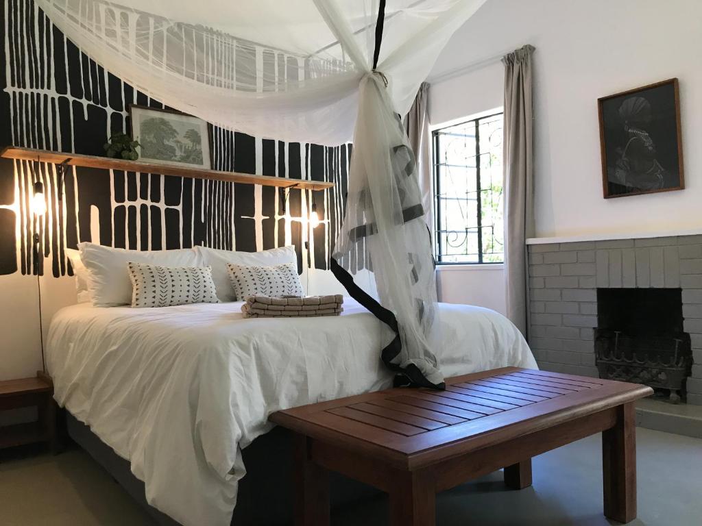 a bedroom with a bed with a table and a fireplace at Birdsong Bungalow in Livingstone