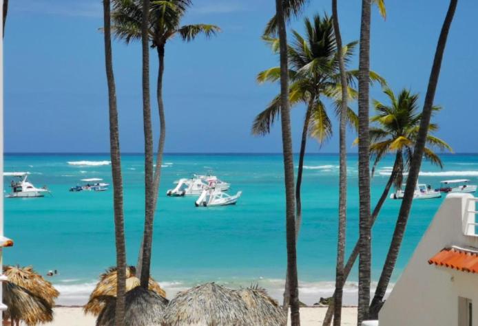 a beach with palm trees and boats in the water at CARIBBEAN DREAMS Apartment & Villas - OCEAN VIEW - POOL - BBQ in Punta Cana