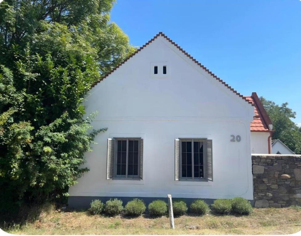a white house with black windows and a stone wall at Rusztikus ház Mindszentkálla in Mindszentkálla