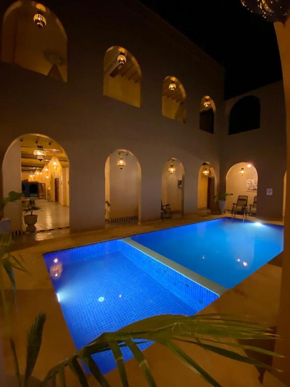 a large swimming pool in a building with a blue pool at Riad Dar Fatima in Merzouga
