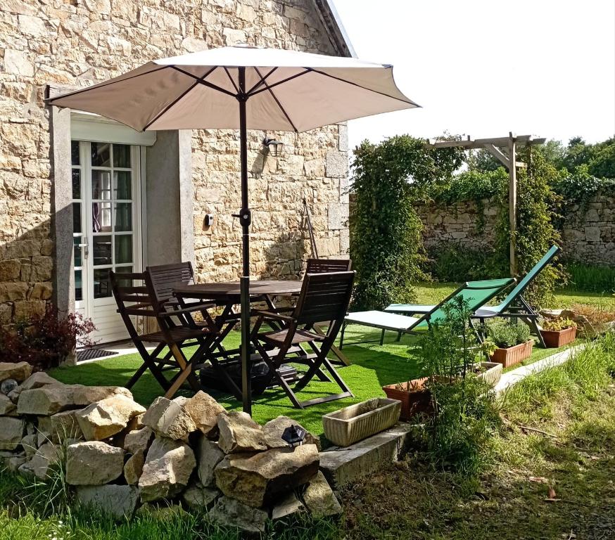 a table and chairs with an umbrella in a yard at Cottage de charme en pierres à 25 mn de la côte de Granit rose in Bégard