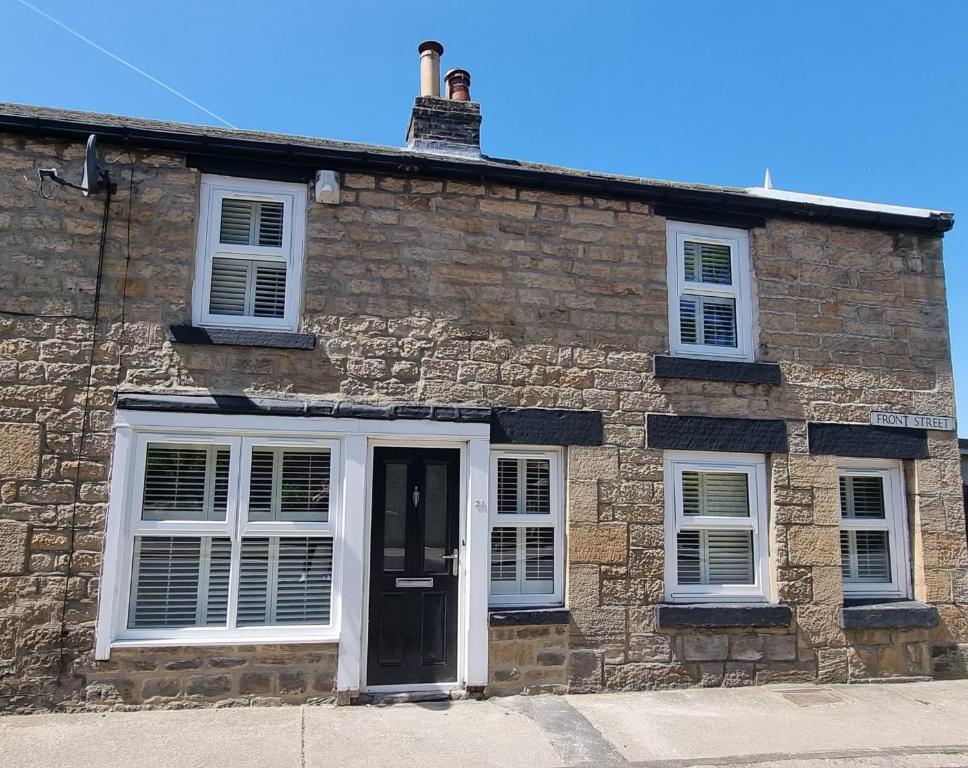 a stone house with white windows and a black door at The Neuk in Shotley Bridge