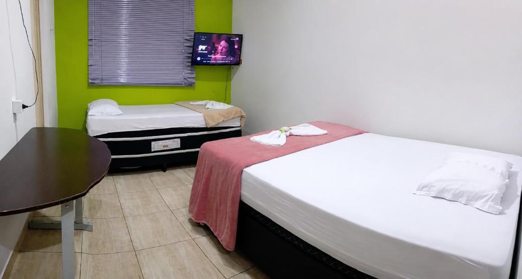 a room with two beds and a table and a table at Jams Hostel - Pousada perto da Ufcat in Catalão
