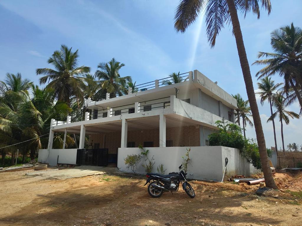 a motorcycle parked in front of a house with palm trees at Hamsa Farmstay - 3BHK AC homestay in Mysore
