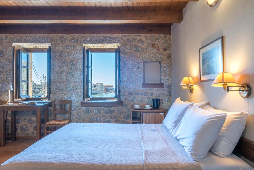 ein Schlafzimmer mit Bett, Schreibtisch und zwei Fenstern in der Unterkunft Pyrgoi Theodorakaki: O Gerolimenas in Yerolimin