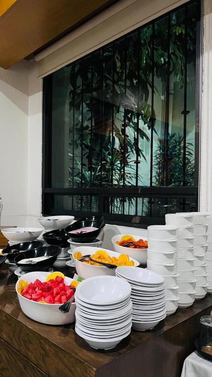 A breakfast counter is crowded with fruit bowls, plates, and stacked cups beside a large window.