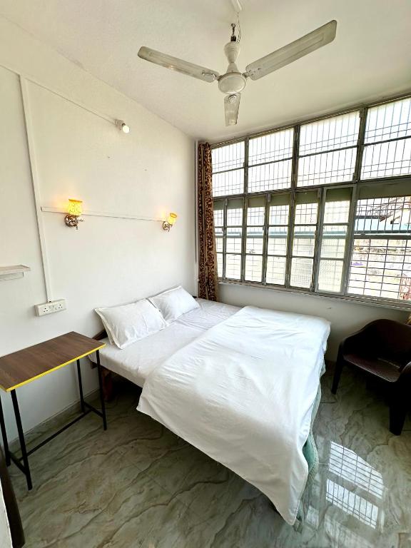 a bedroom with two beds and a desk and windows at Om Rest House by Bunny Cafe Varanasi in Varanasi
